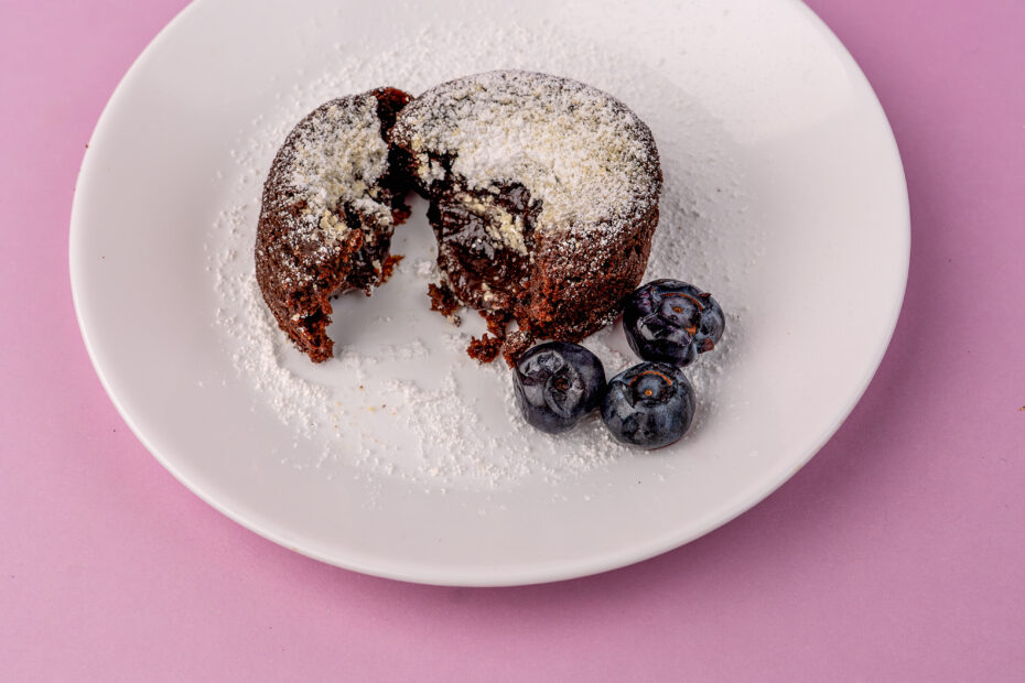 Volcán de chocolate con arándanos, con exterior suave y centro líquido de chocolate que se mezcla con arándanos jugosos, servido caliente en un plato con presentación casera y apetecible.